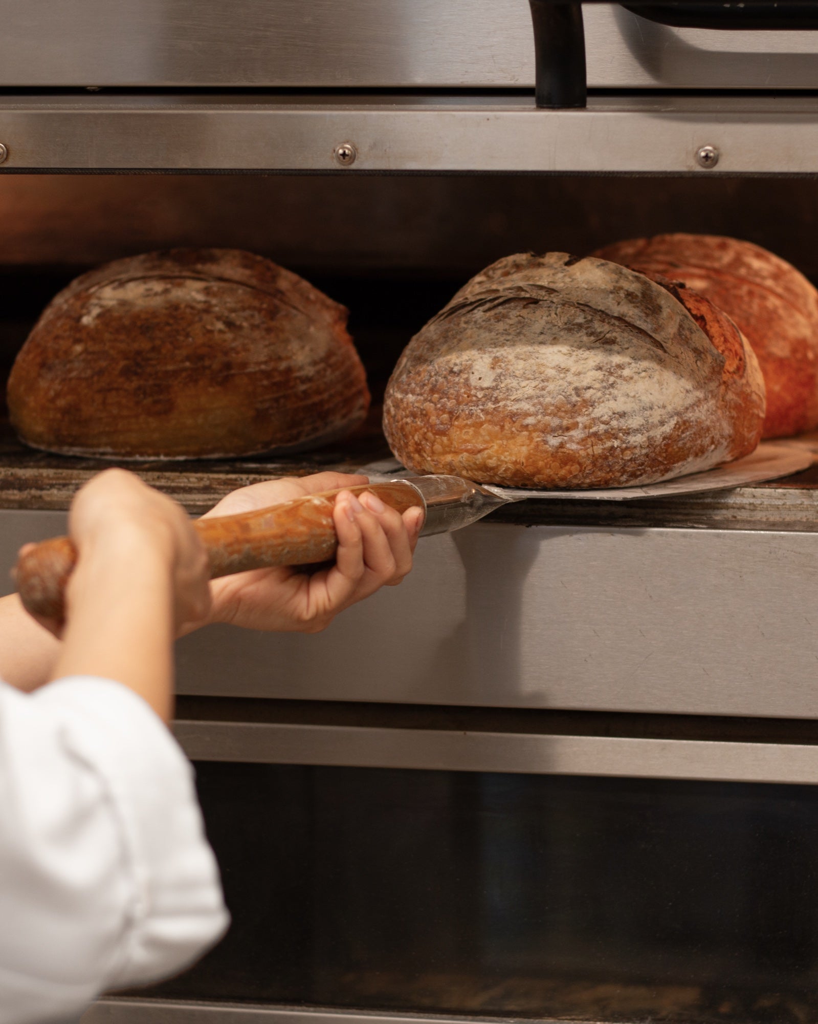 A Pantry d’Or baker taking freshly baked sourdough out of the oven